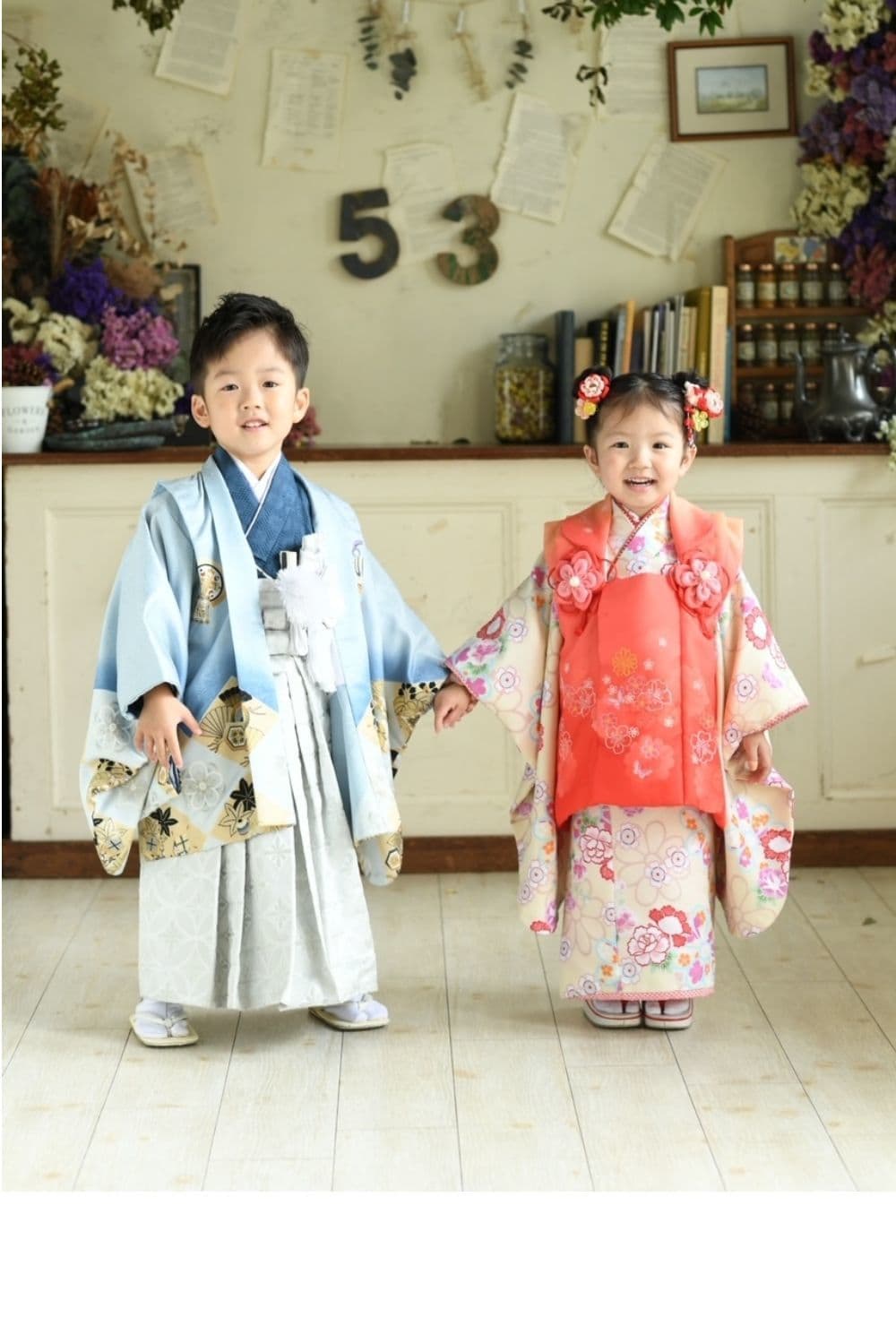 水色の羽織で白袴を着た男の子とピンクの肩上げ着物と被布コートを着た女の子が手をつないでいる